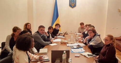 Meeting of people around a long table with Ukrainian flag in the background